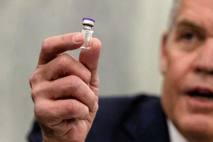 A man wearing a suit holds up a vial of liquid.