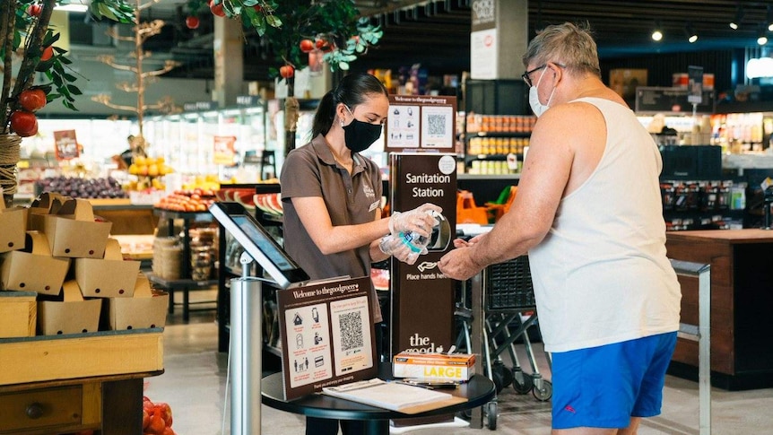 A woman gives a man hand sanitiser at a supermarket.