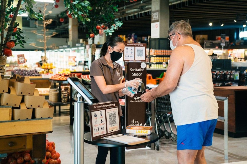 A woman gives a man hand sanitiser at a supermarket.