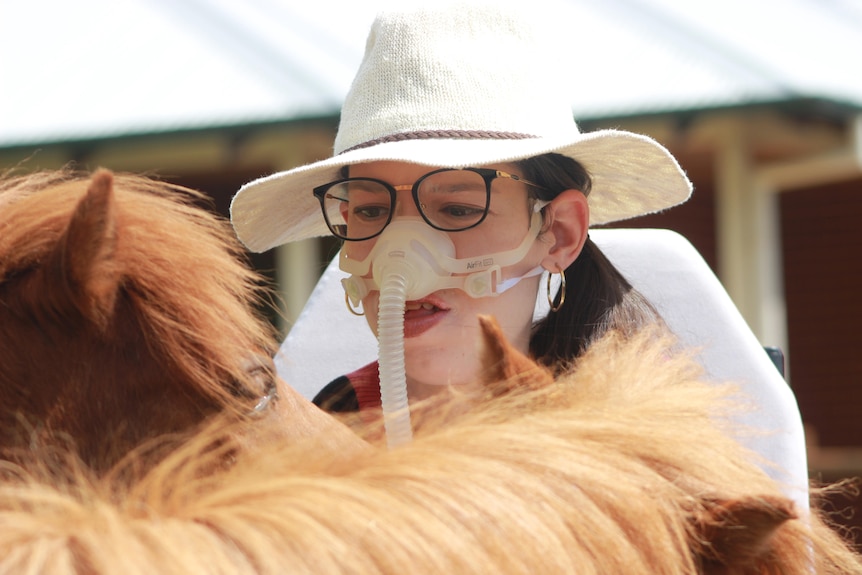 A close-up shot of Amy Evans wearing a ventilator and attending to a miniature horse.