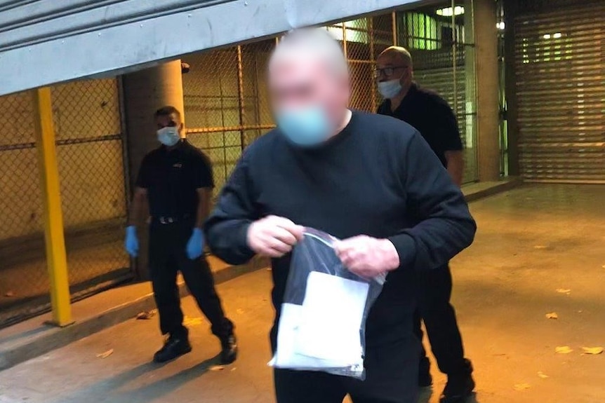 A man wearing a mask,whose face is pixelated, leaves court carrying a plastic bag.