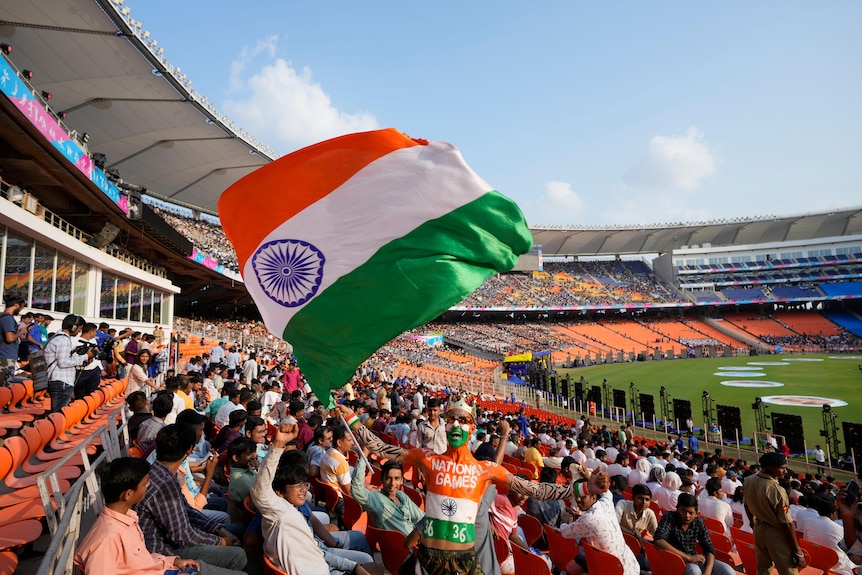 A man painted in the colors of the Indian flag waves the Indian flag in the crowd at Narendra Modi Stadium.