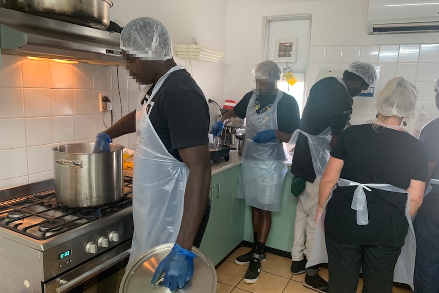 A group of people wearing hair nets and aprons cooking in an industrial kitchen.