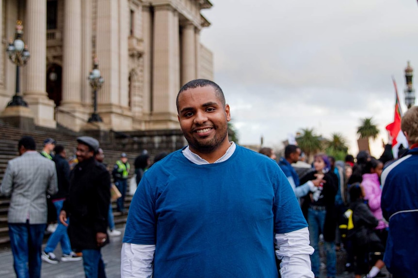 A man in front of the Victorian parliament wears a royal blue shirt in front of a crowd.