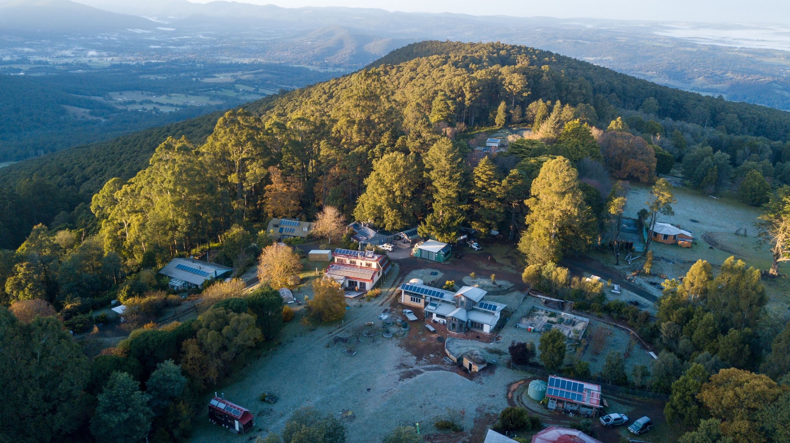 An aerial image of a small community on a hilltop surrounded by forest.