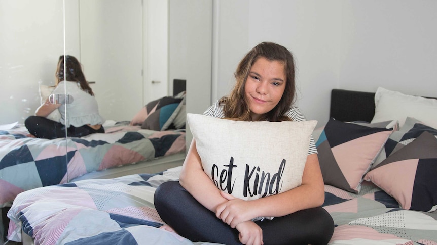 Monique Mastrobattista sitting on her bed with a Get Kind cushion
