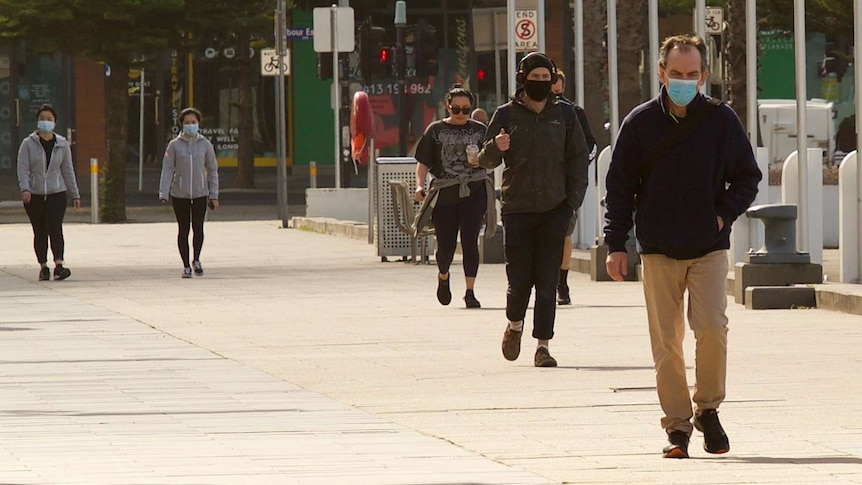 People in face coverings and long-sleeved shirts walk along a footpath in Docklands.