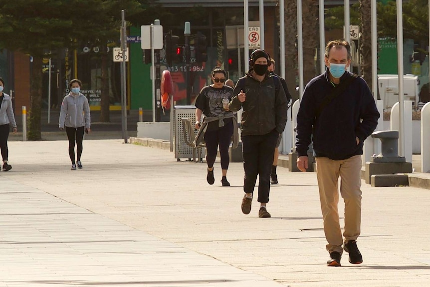 People in face coverings and long-sleeved shirts walk along a footpath in Docklands.