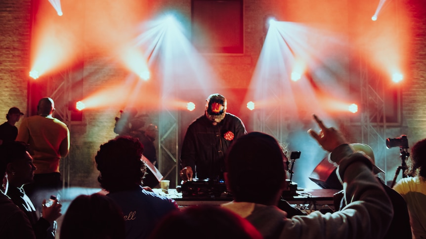 A DJ looks down at his decks as he performs in front of a crowd. 