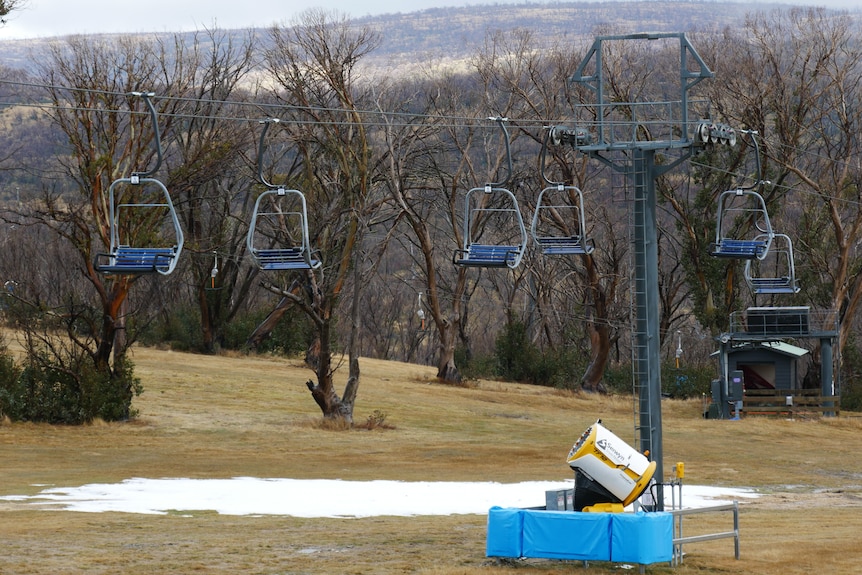 a small patch of snow on a hilldside, with a snow gun and empty chairlift