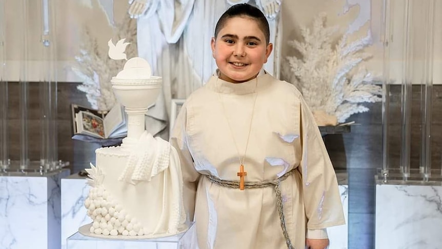 a young boy dressed in altar server gear standing next to a figurine of a chalice