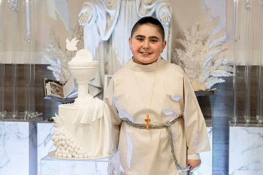 a young boy dressed in altar server gear standing next to a figurine of a chalice