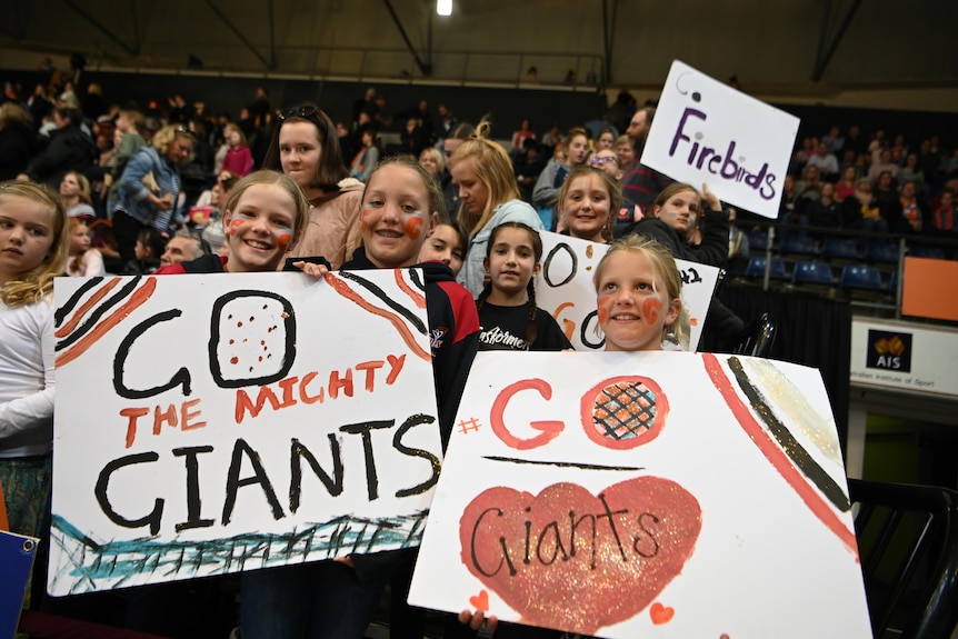 Young girls wait to meet netball players with their cardboard signs