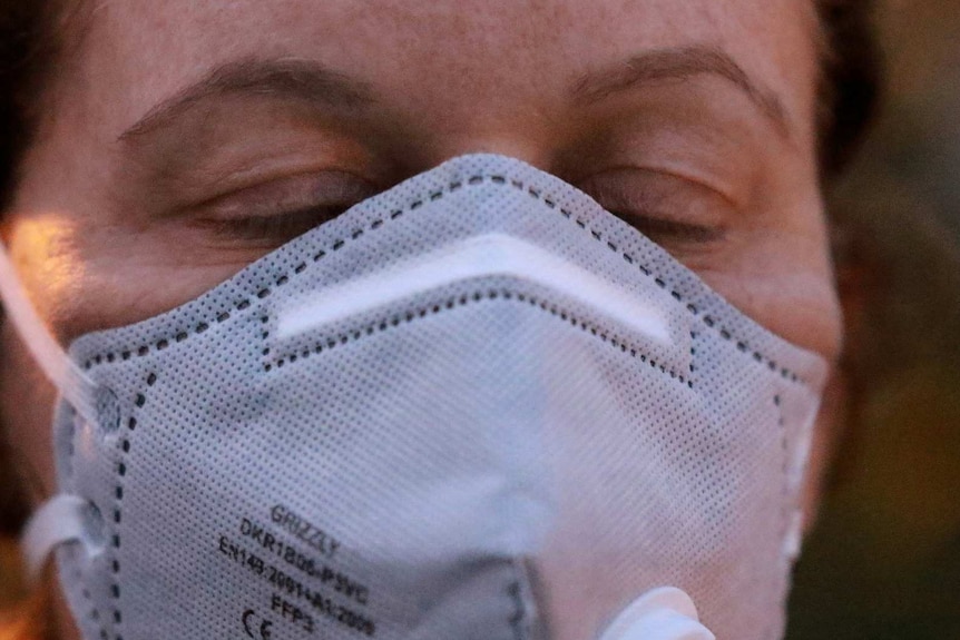 Unidentified female wearing a respiratory mask, with eyes closed.