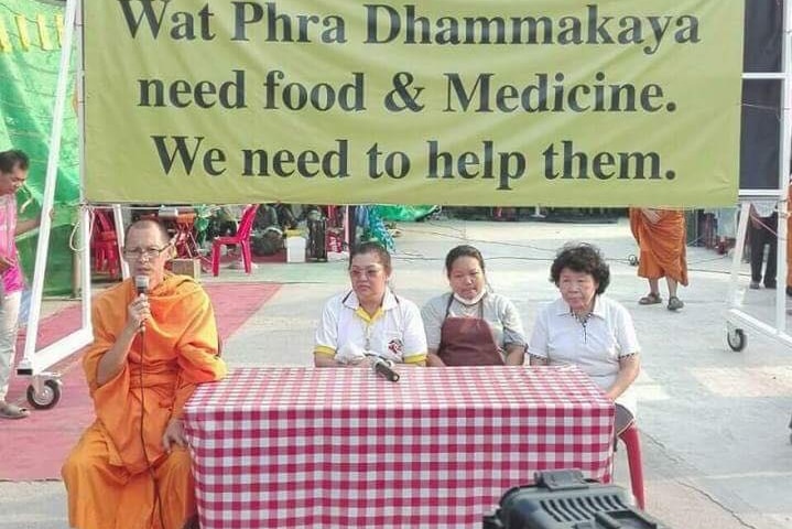 The Dhammakaya sect of Thai Buddhism members sit in front of a sign explaining why their founder is facing a number of charges
