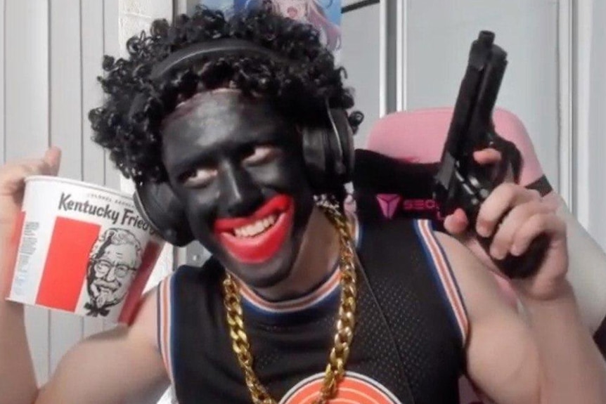 A man doing blackface, holding up a KFC bucket and a gun