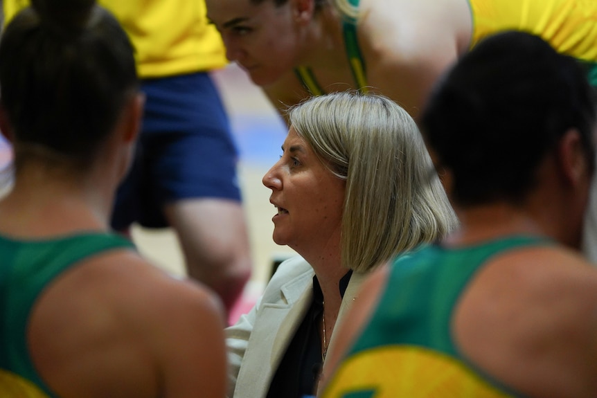 The image focuses on a Australian netball coach talking while surrounded by her players during a match.