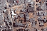A close view from above of a building complex completely knocked down into rubble, with roads and the ground becoming dirt