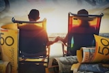 A couple hold hands while sitting on chairs at the beach