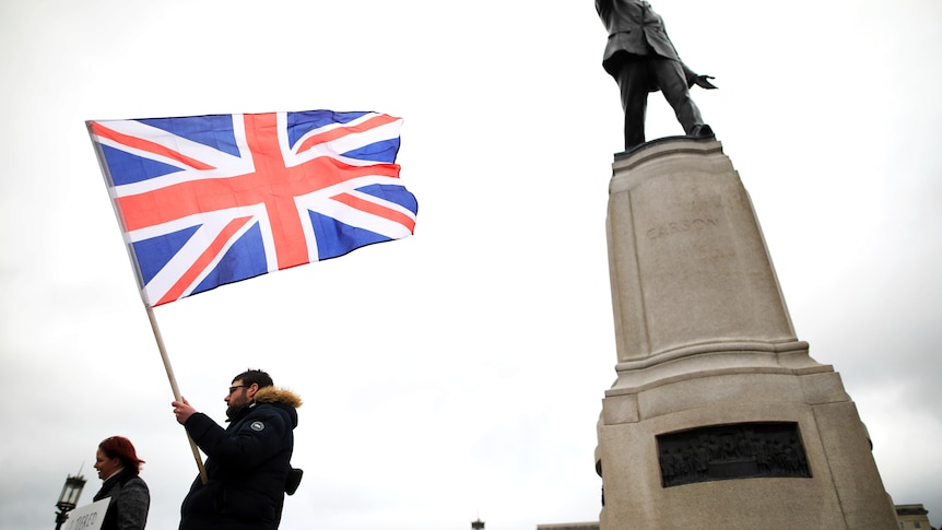 Two people standing near a statue and holding the Britain flag.