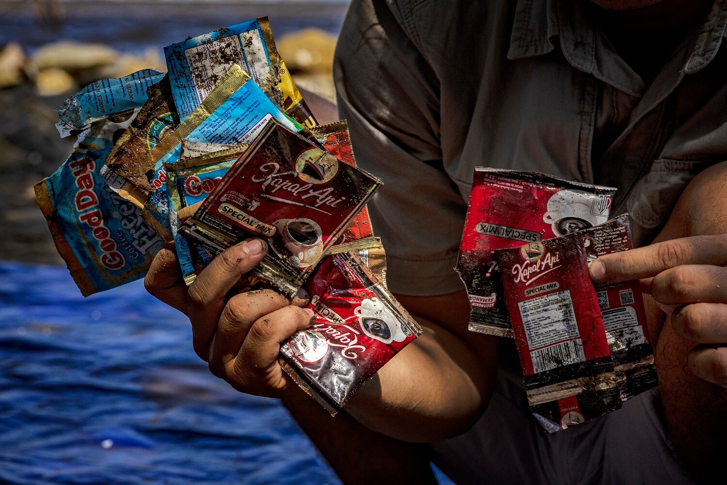 Close up photo of two hands holding several plastic sachets of instant coffee.