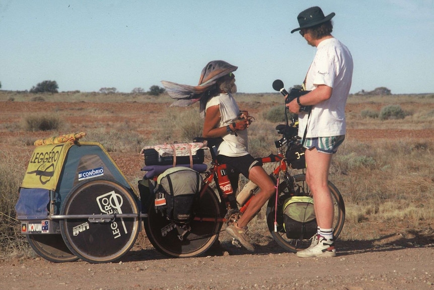 Cyclist with packed up bicycle and trailer being interviewed by tall man with microphone