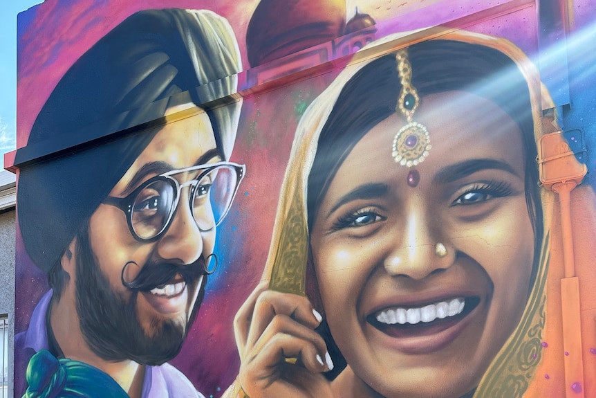 A painted mural of a smiling woman wearing a headscarf and jewellery piece, a man and a child in turbans.