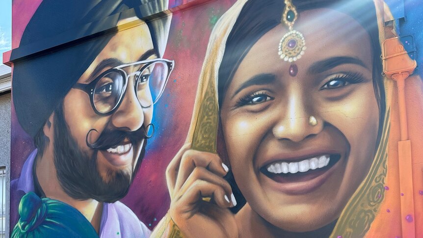 A painted mural of a smiling woman wearing a headscarf and jewellery piece, a man and a child in turbans.