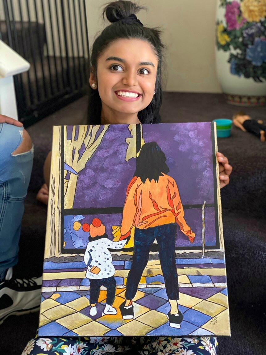 Falak smiles while holding a painting in front of her.