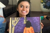 Falak smiles while holding a painting in front of her.