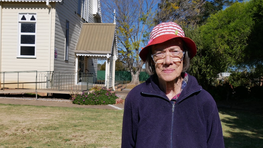 An elderly lady wearing a purple jacket and a red and white striped hat standing outside a church.