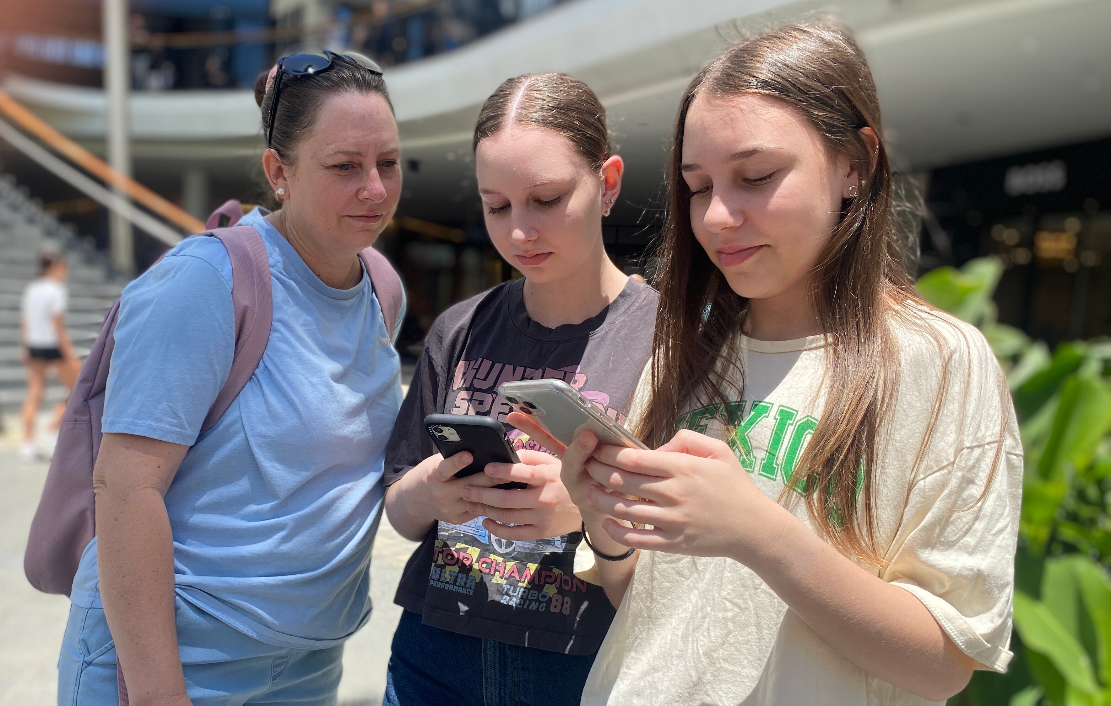 A mother looks over the shoulder of her daughters who are checking their phones.