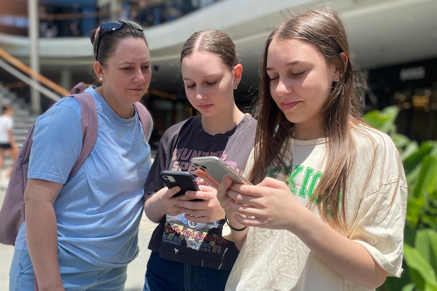 A mother looks over the shoulder of her daughters who are checking their phones.