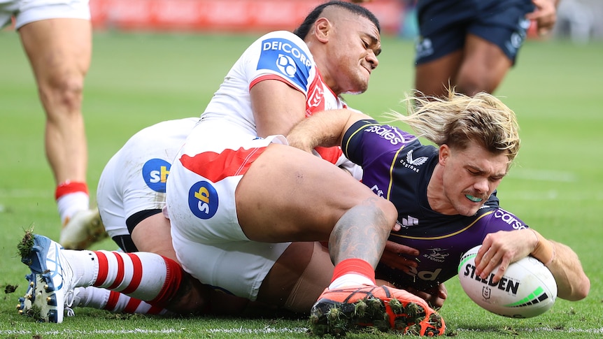 A Melbourne Storm NRL player scores a try while being tackled by a St George Illawarra opponent.