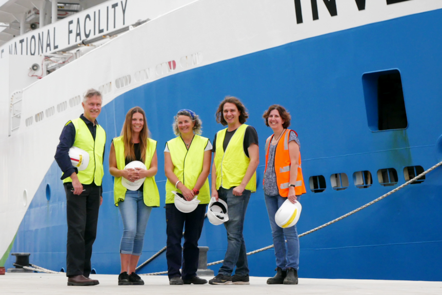 Researchers stand in hi-vis vests in front of a boat.