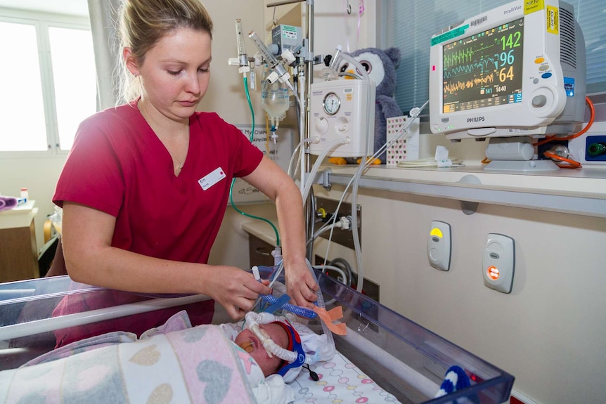 A nurse fixes the breathing tube of a baby