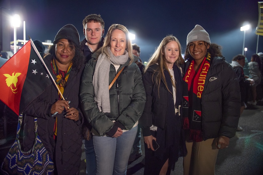 A group of rugby league fans with PNG colours in front of a stadium at night
