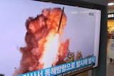 A man with a cleaning cart in a shopping watches television footage of a missile being launched.