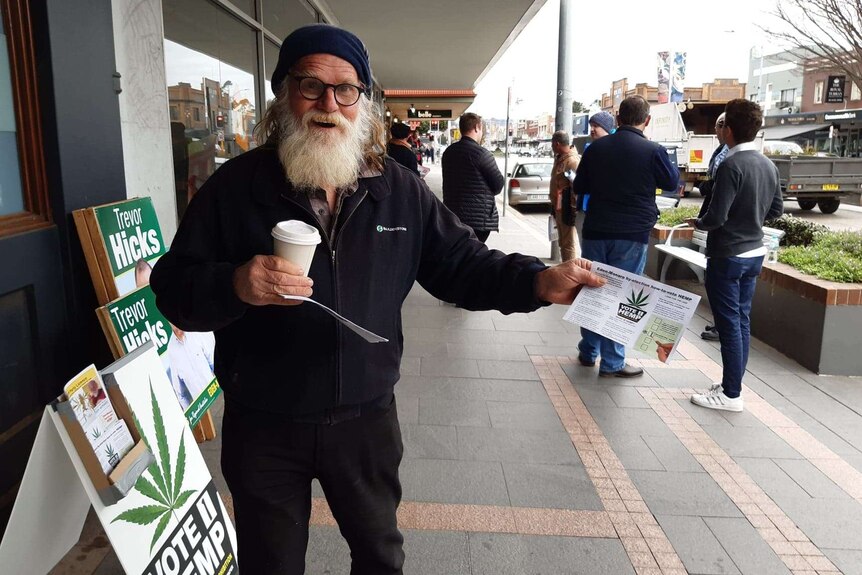 Michael Balderstone holding a coffee cup and handing out voting guides for the Hemp Party