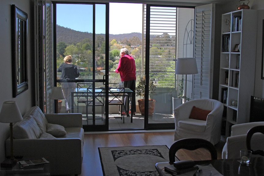 Husband and wife overlook balcony outside with a view of Mount Ainslie.