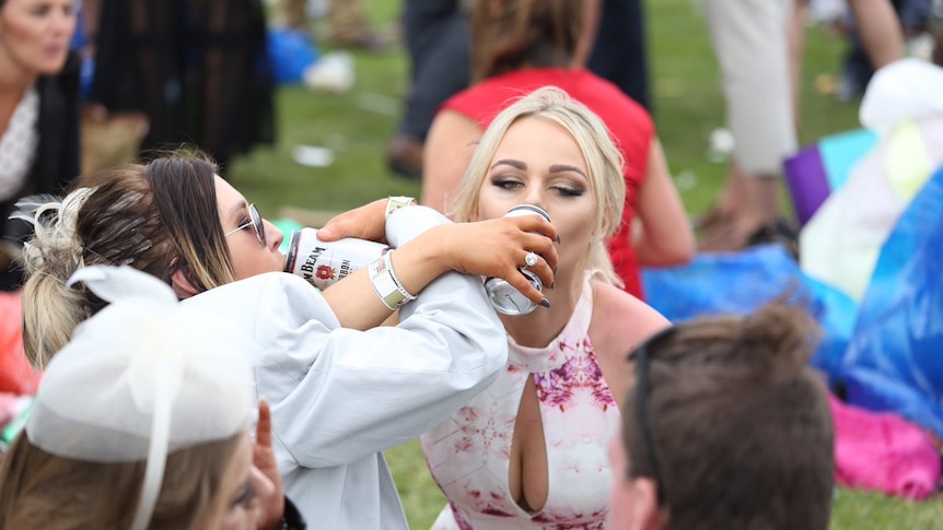 Two girls, linked in arms and drinking alcohol.