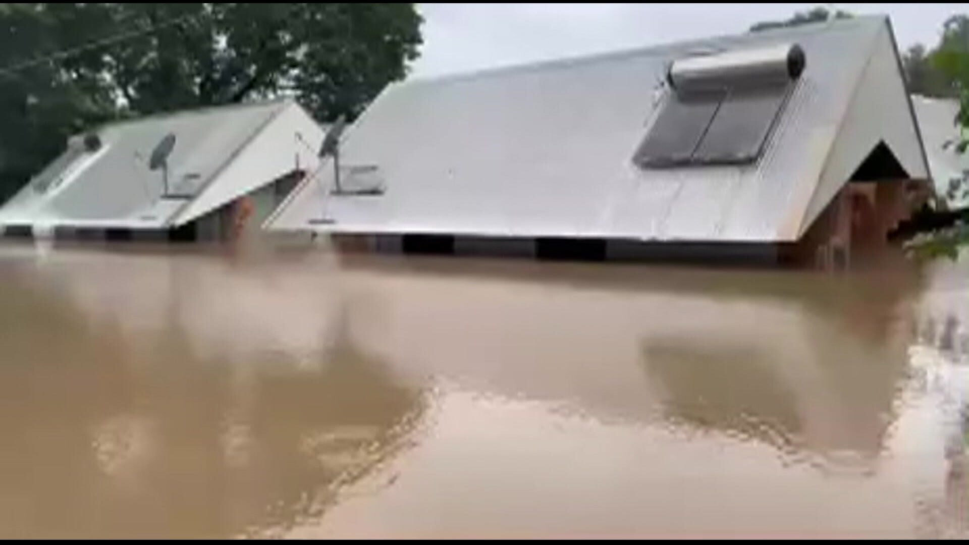 Grainy image of two homes with brown flood water just below its roof.