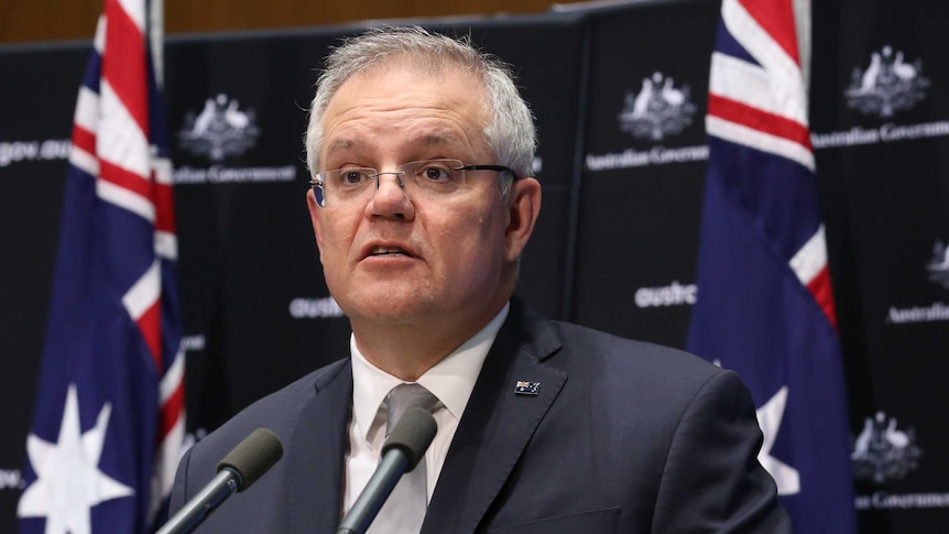 Scott Morrison talks at a lectern in front of two flags