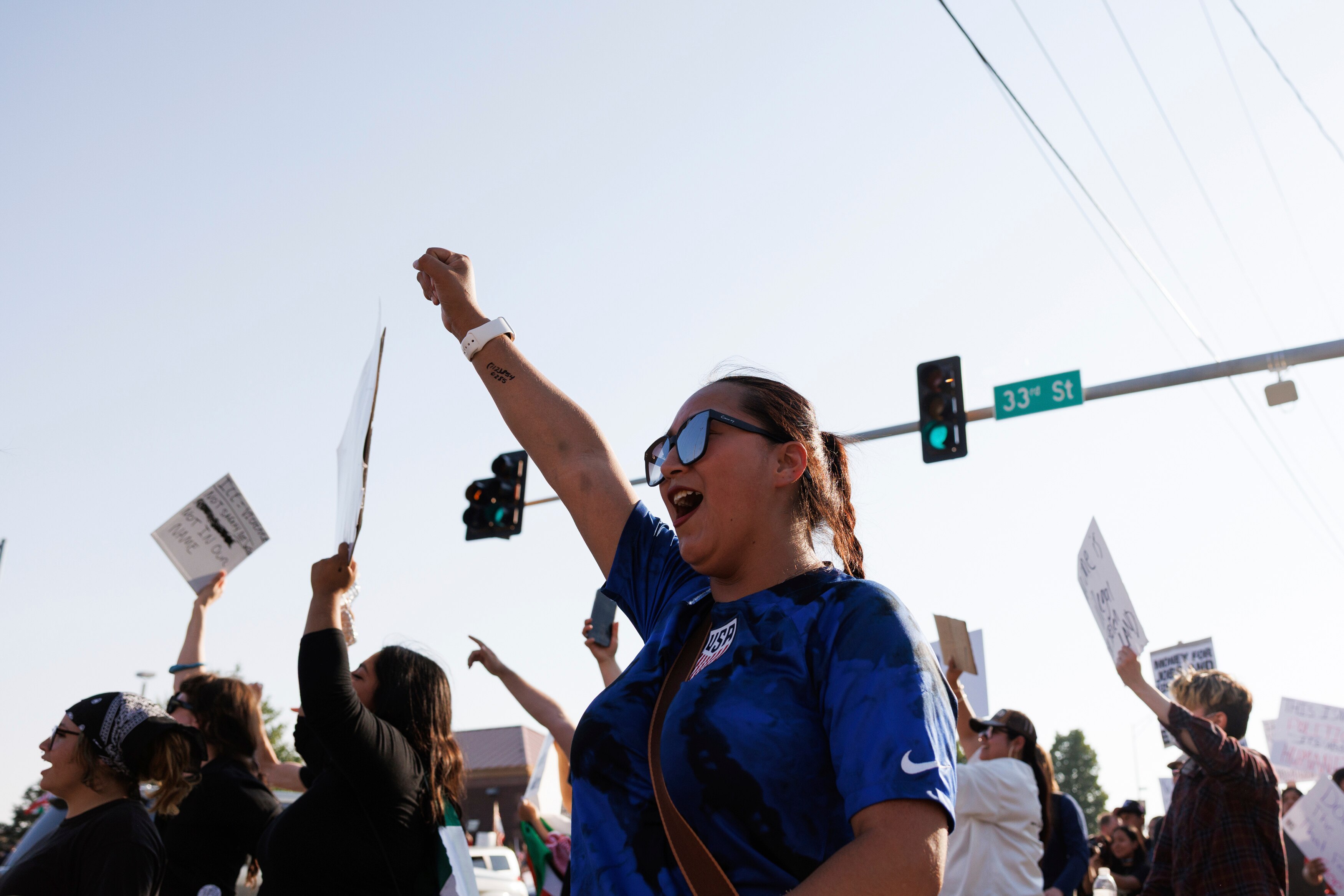 A woman holding her fist up chanting in a crowd walking down a road.