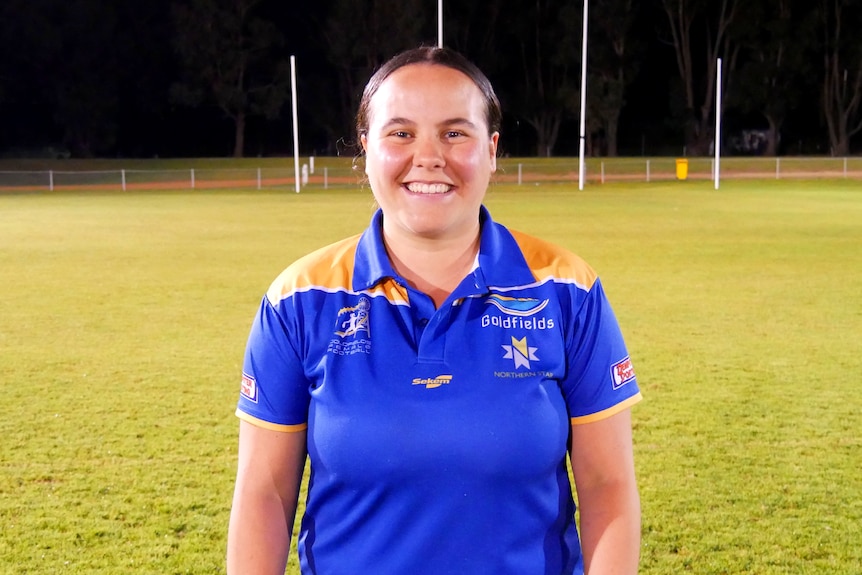 A woman standing in the middle of a football oval.