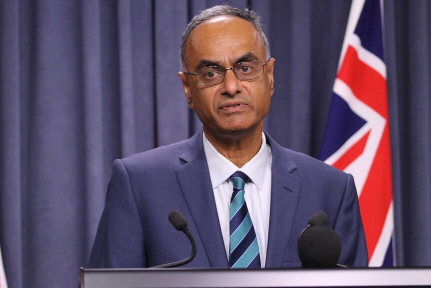 A mid shot of WA chief health officer Tarun Weeramanthri speaking ata  media conference in front of an Australian flag.