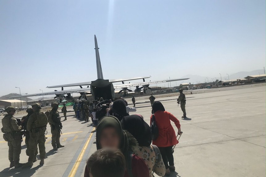 military personnel and people are waiting on the tarmac in front of a military aircraft at Kabul airport