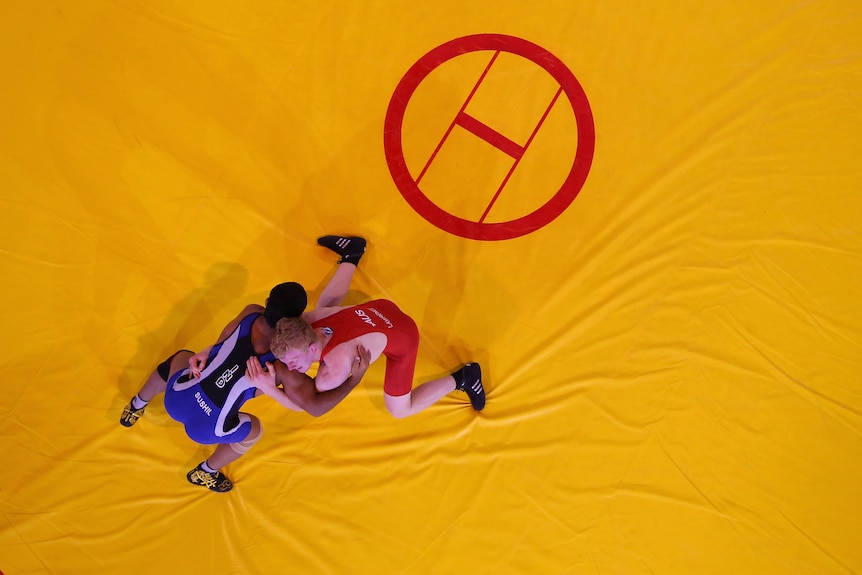 Two wrestlers, one wearing blue and one wearing red, compete on a yellow mat