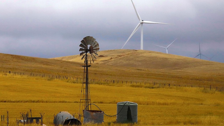An old windmill stands in front of wind turbines in a paddock near the Hornsdale Power Reserve, South Australia