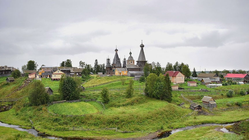 An old Russian town stands behind bright green fields.